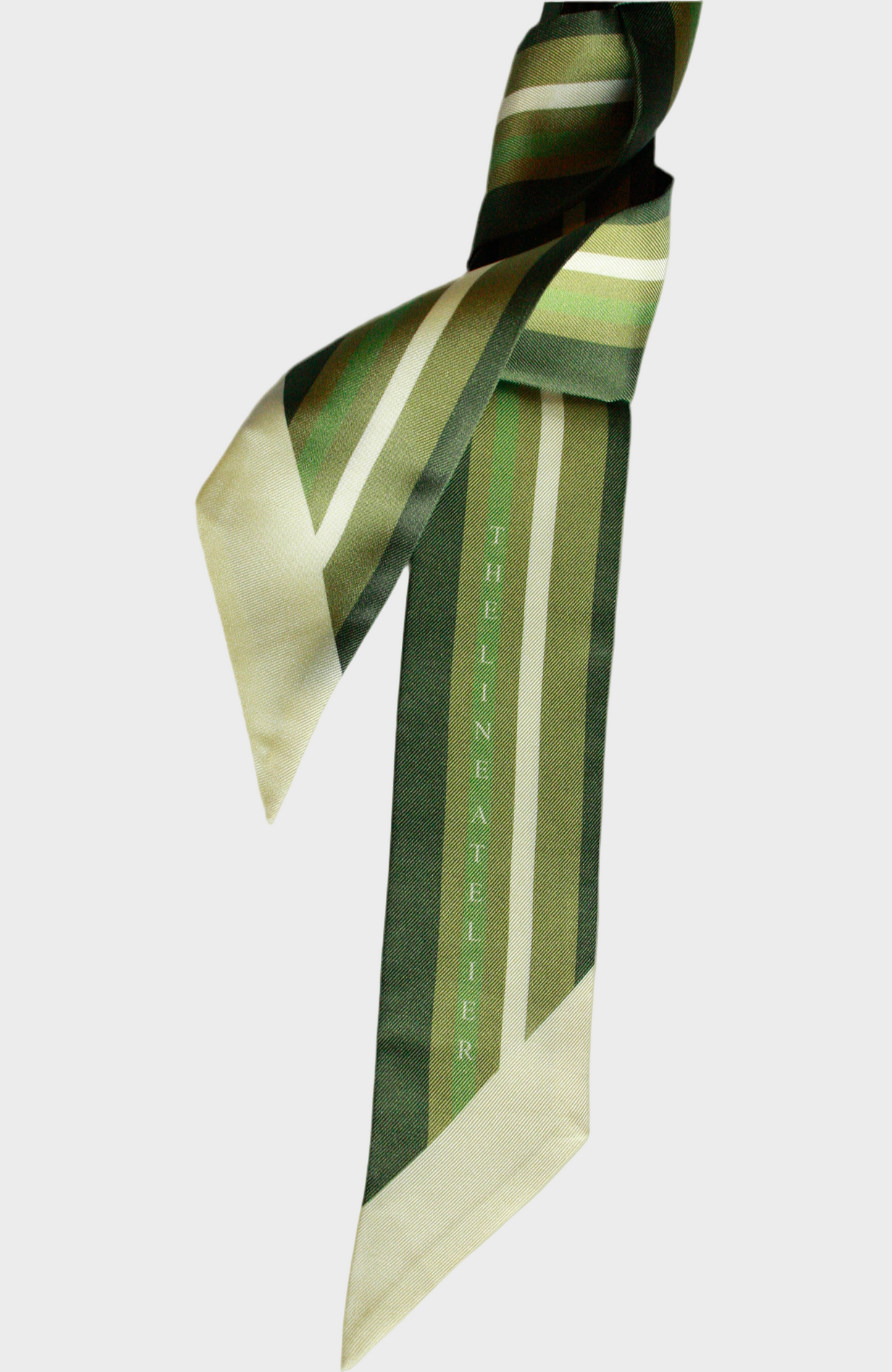 Green and beige striped twilly silk scarf with 'The Line Atelier' branding on a beige background