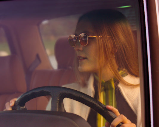 Woman driving a car with a blurred background wearing silk twilly scarf