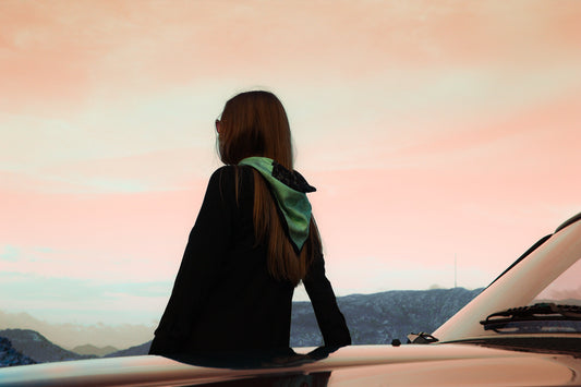 Person standing by a car with a scenic view in the background wearing Ballet - The Poised Rogue 60x60cm cool green silk scarf with black ballerina lineart