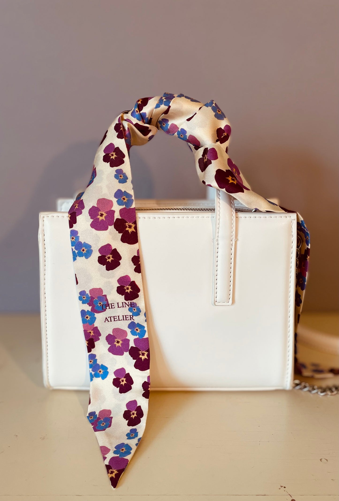 Floral scarf draped over a white handbag on a neutral background
