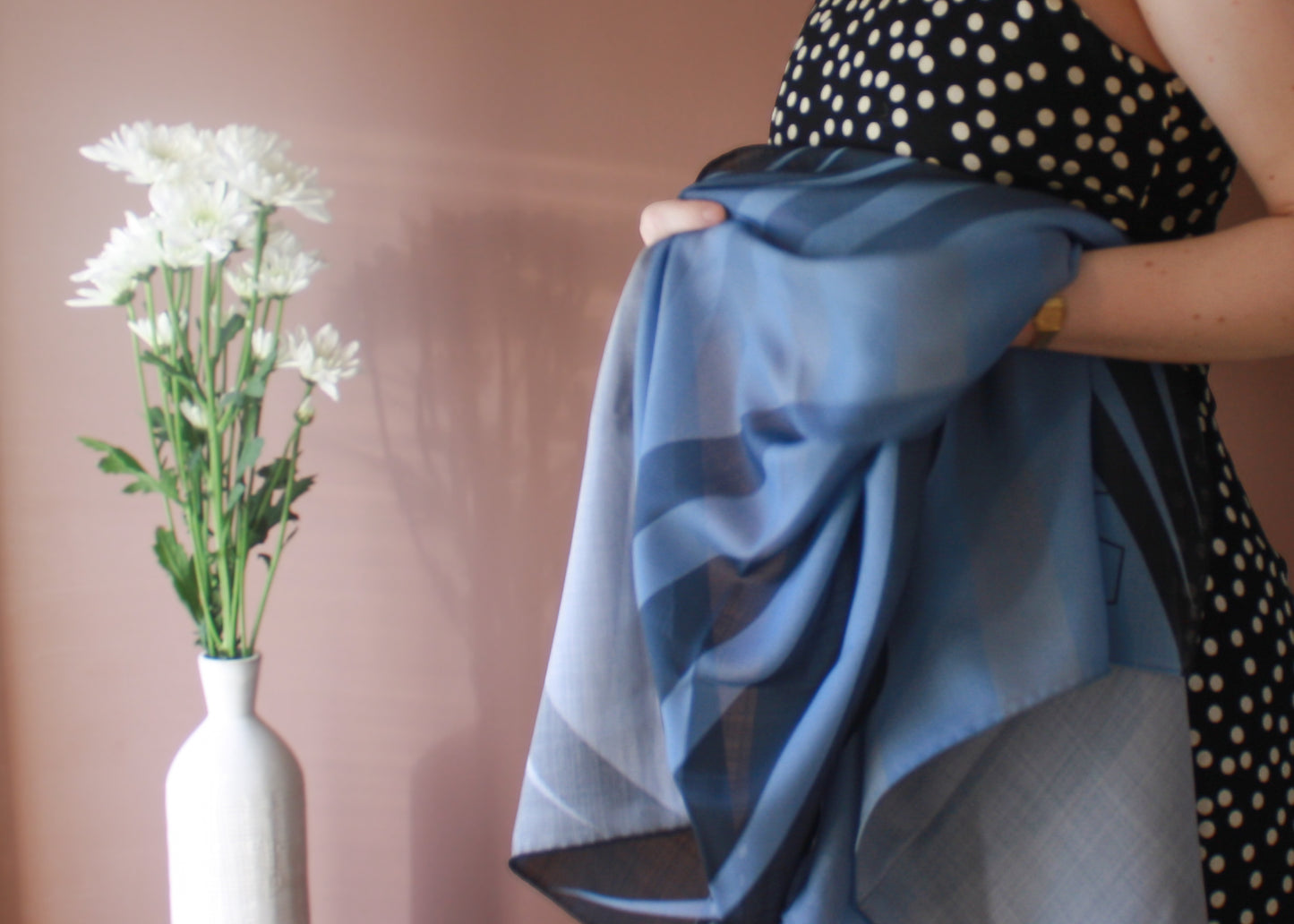 Model holding Ice Valley Wool and Silk Scarf by The Line Atelier with a vase of white flowers on a pink background