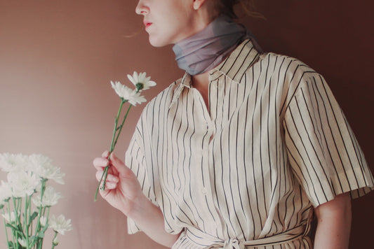 Model wearing Love Potion nr 9 Silk & Wool scarf by The Line Atelier holding flowers next to a vase on a table.