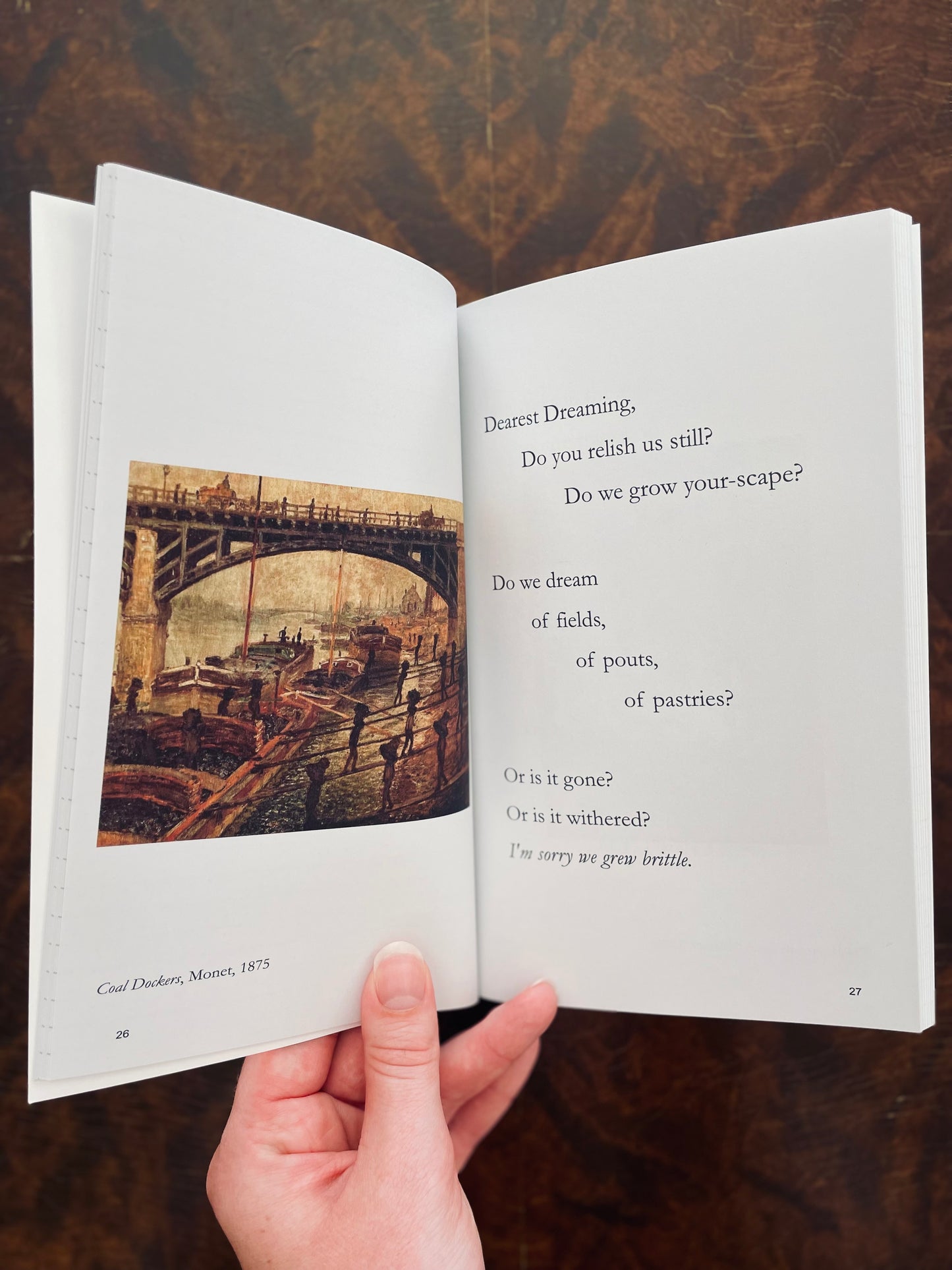 Open Of Shallows & Depths Journal Book with a poem and a painting held by a hand on a wooden surface