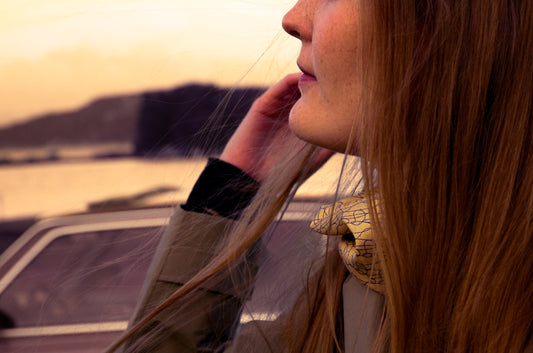 Woman with long hair against a sunset landscape wearing beige silk scarf
