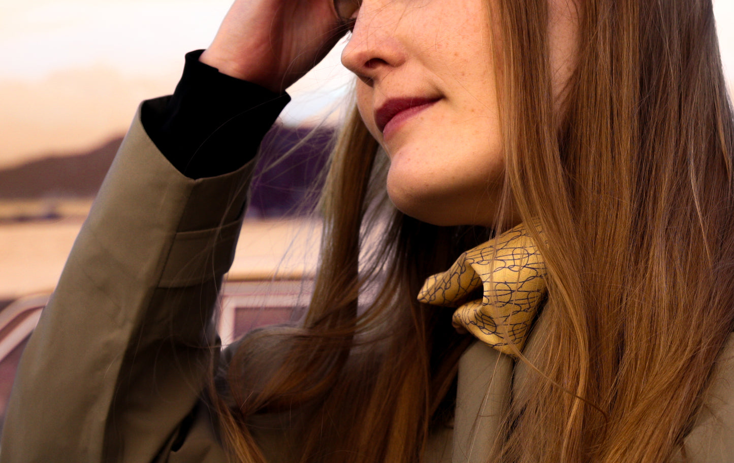 Woman with long hair against a sunset landscape wearing beige silk scarf