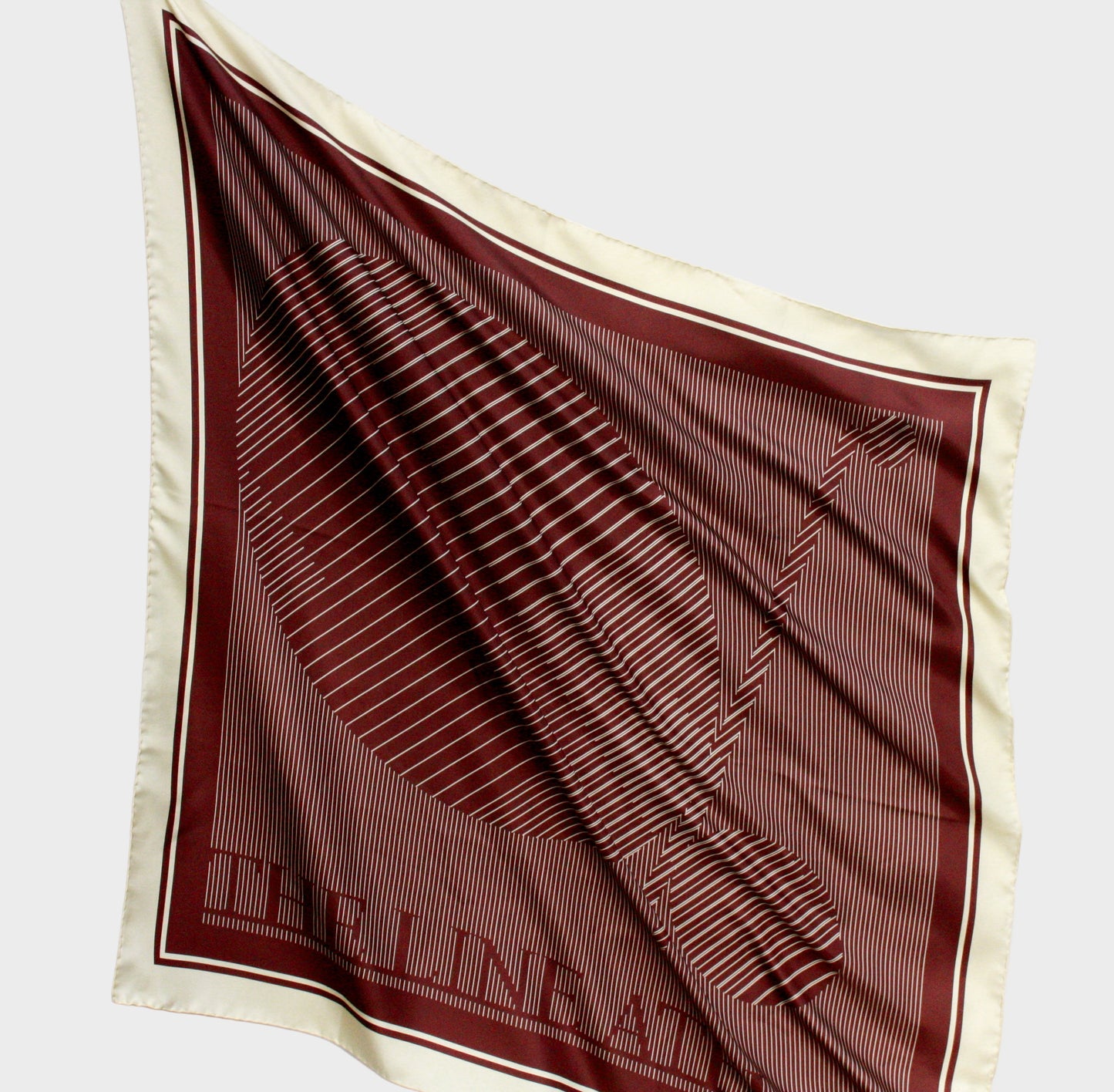 Brown and beige patterned silk scarf with 'The Line Atelier' label on a light gray background