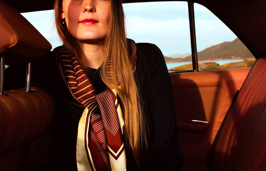 Woman sitting in a car with a scenic background wearing a large brown silk scarf