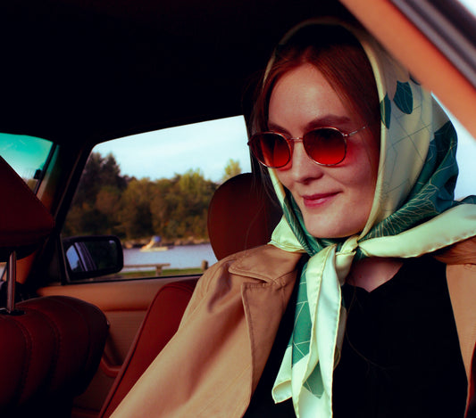 Woman wearing a headscarf and sunglasses sitting in a car with a scenic background