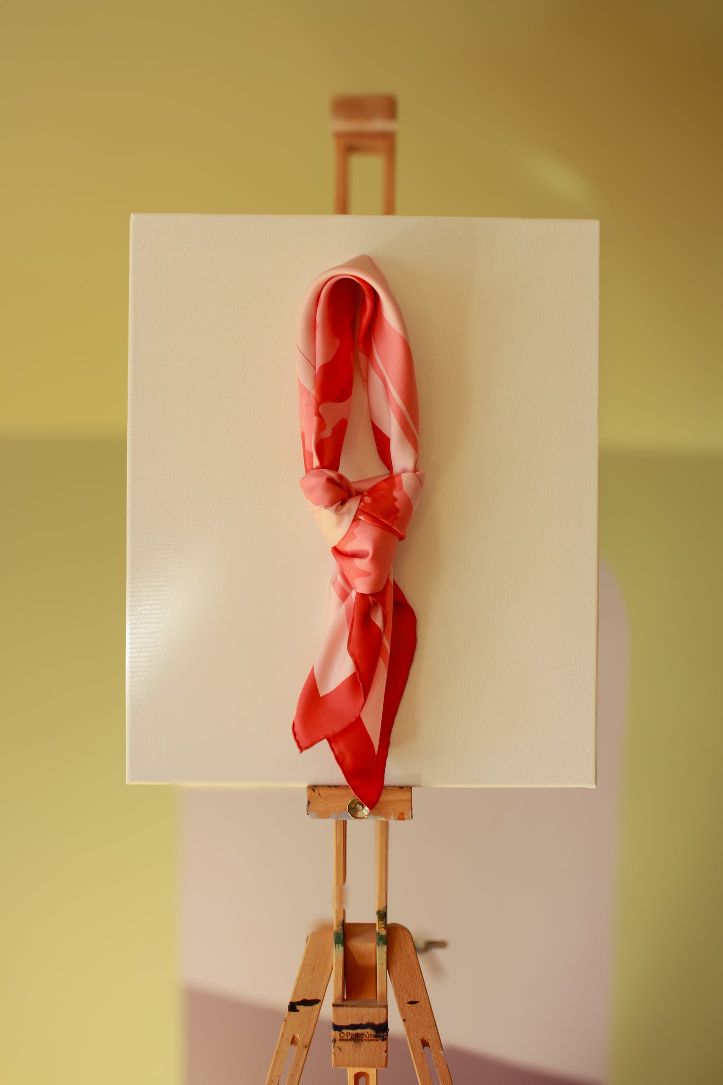 Rose d`Amour silk scarf on a wooden easel against a green wall
