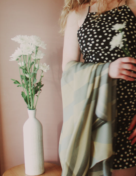 Model holding Willow Grove Wool & Silk Scarf by The Line Atelier next to a vase with white flowers against a pink wall