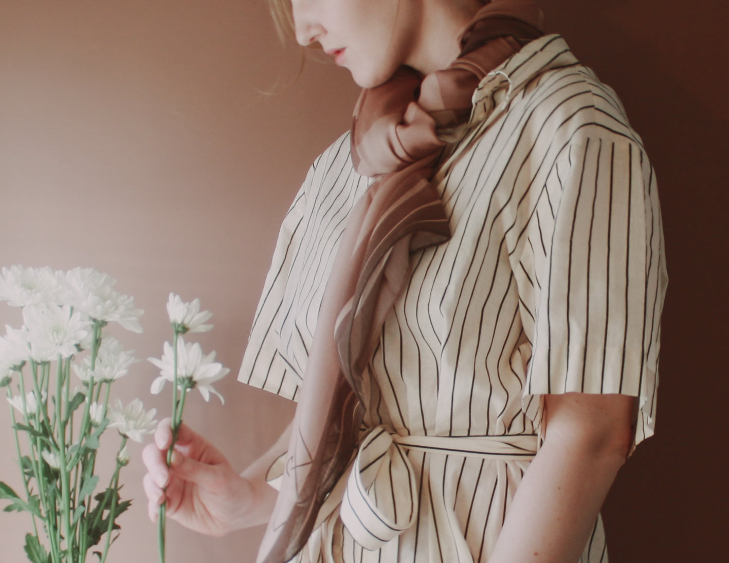 Model wearing Bronze Sandrift Wool & Silk Scarf holding flowers against a warm-toned background