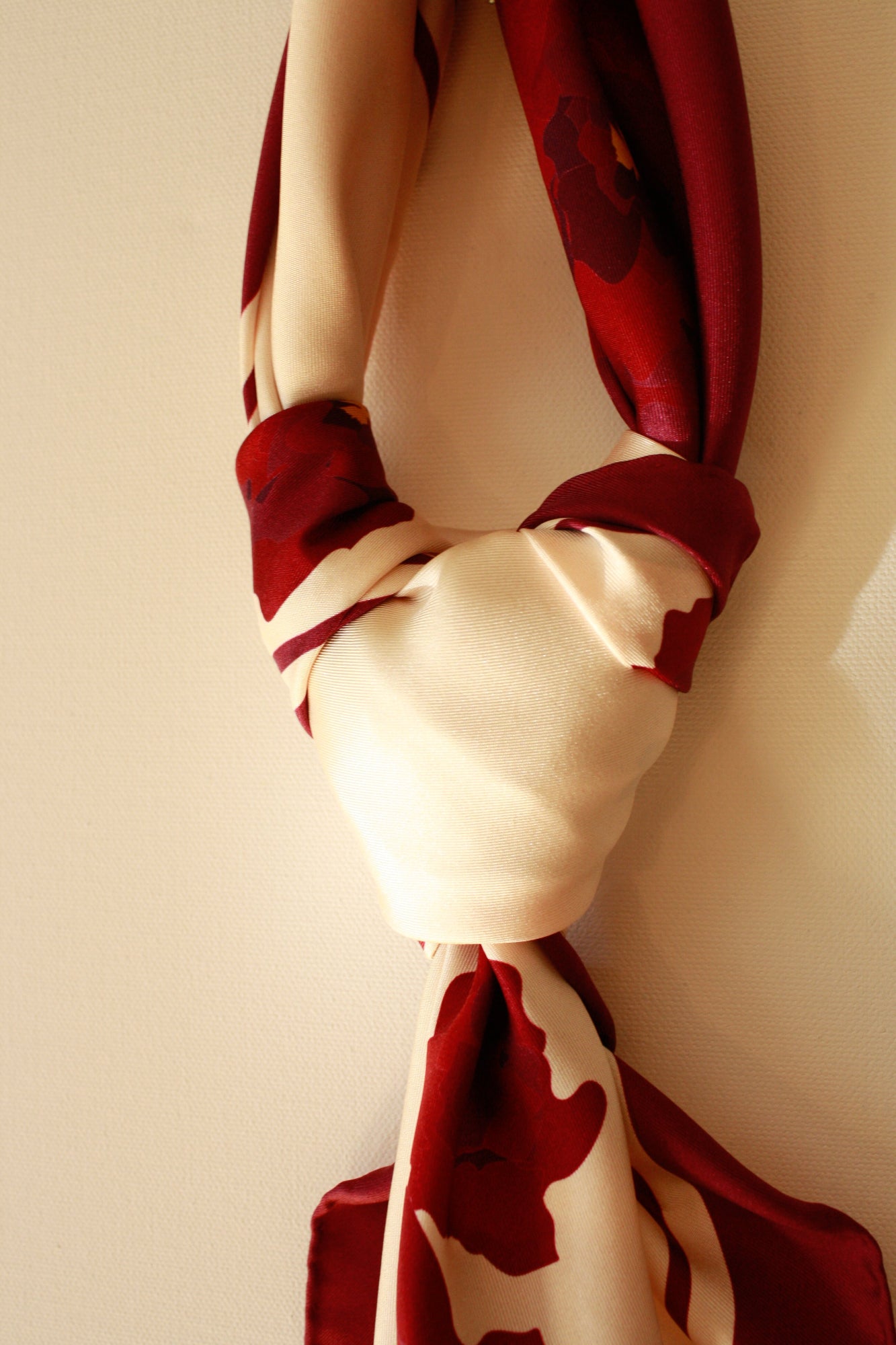 Close-up of a Cabernet Bloom silk scarf tied in a knot against a beige canvas background