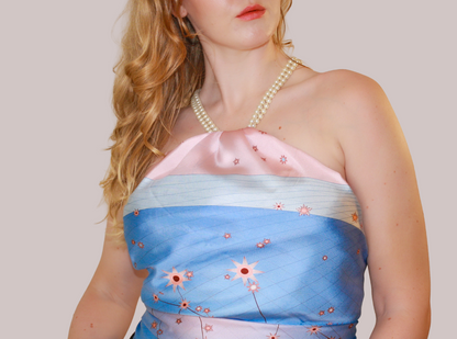 A close-up of a woman wearing Gemini Lovers silk scarf as a top. The scarf features a light pink upper section, a light blue middle section with decorated with pink stars, the Gemini constellation and a pale lavender lower section.