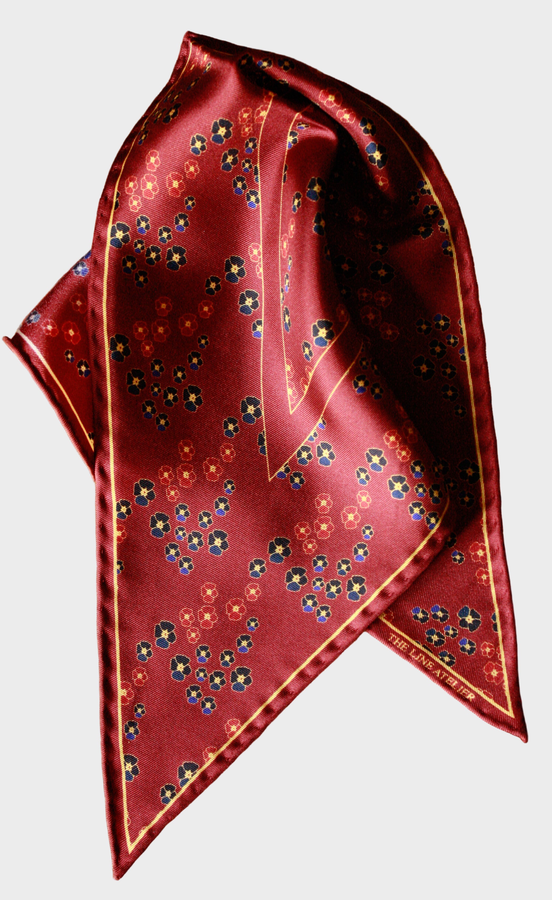 Folded red silk diamond scarf with floral pattern on a beige background