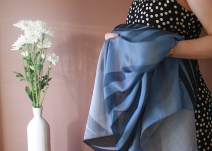 Model holding Ice Valley Wool and  Silk Scarf by The Line Atelier with a vase of white flowers on a pink background