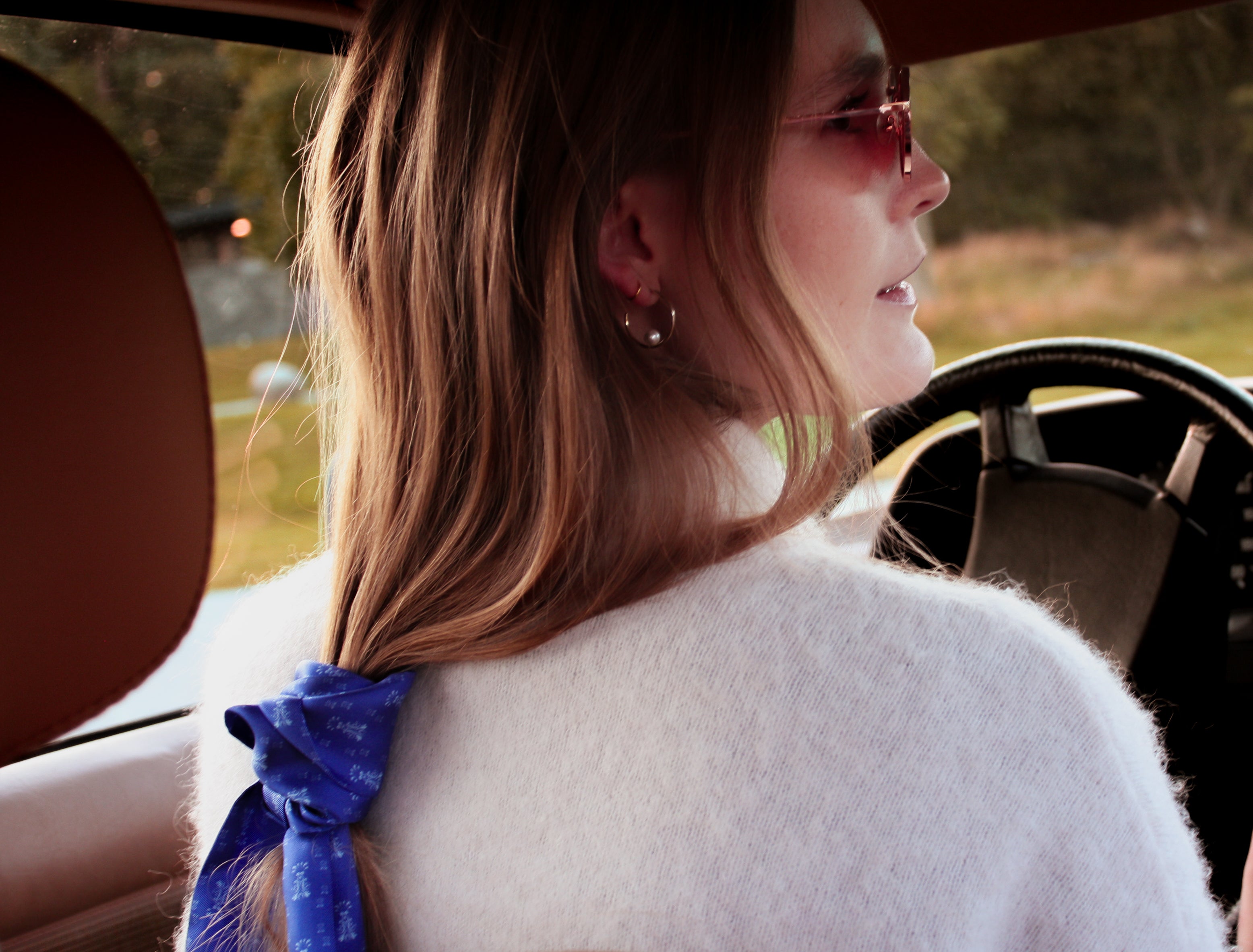 Woman sitting in a car with a scenic view outside wearing blue silk twilly scarf by The Line Atelier