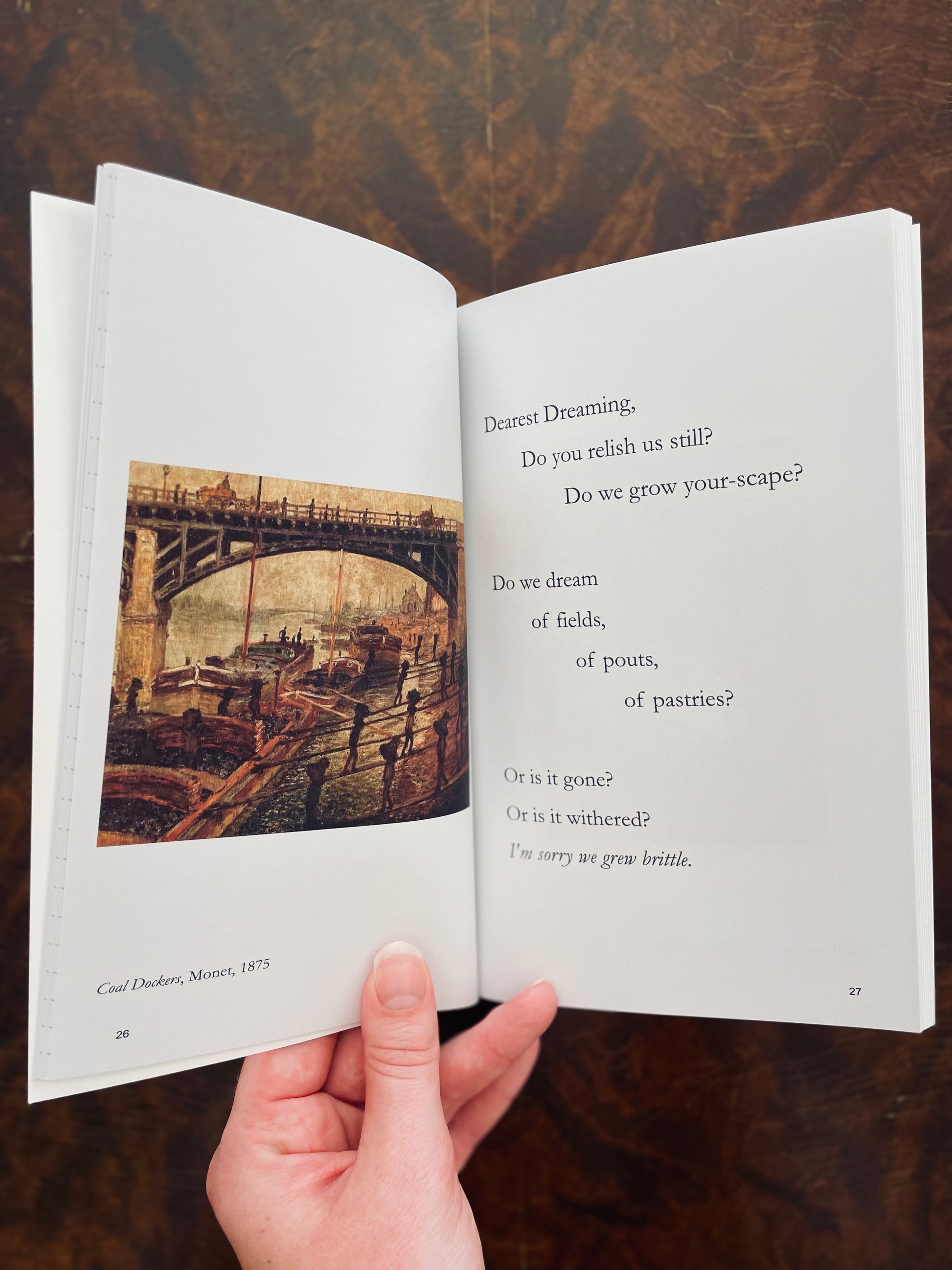 Open Of Shallows & Depths Journal Book with a poem and a painting held by a hand on a wooden surface