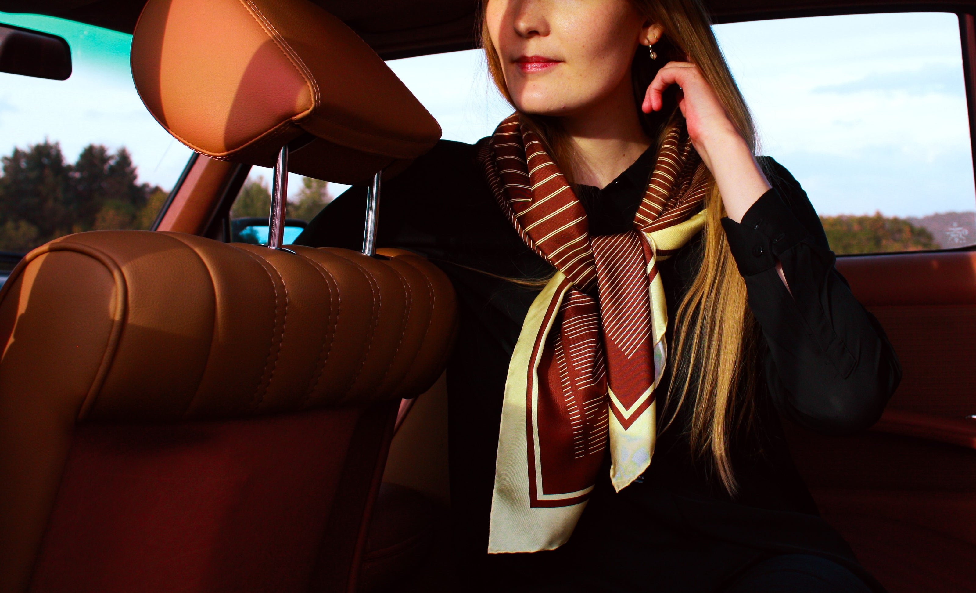 Woman sitting in a car with a patterned scarf, blurred outdoor background