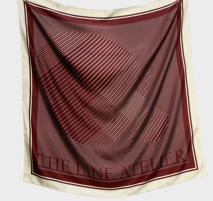 Maroon and beige scarf with 'The Line Atelier' branding on a light gray background
