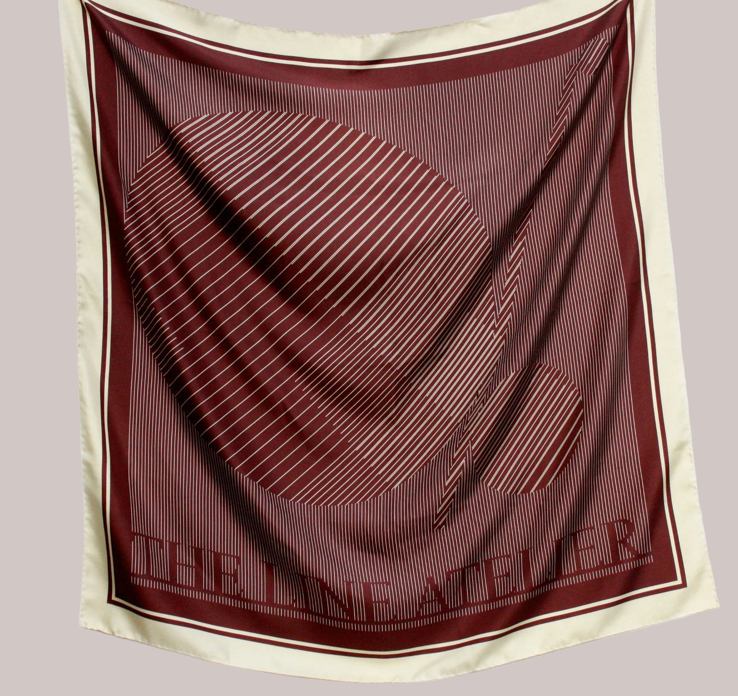 Maroon and beige scarf with 'The Line Atelier' branding on a light gray background