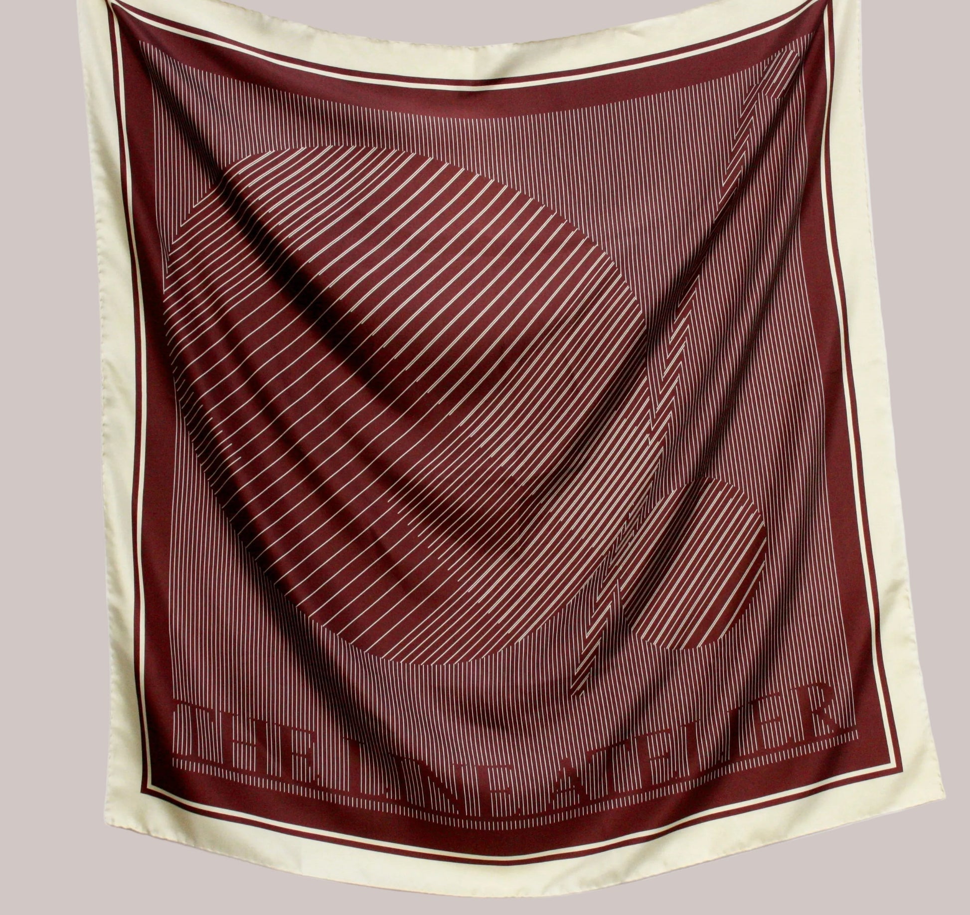Maroon and beige scarf with 'The Line Atelier' branding on a light gray background