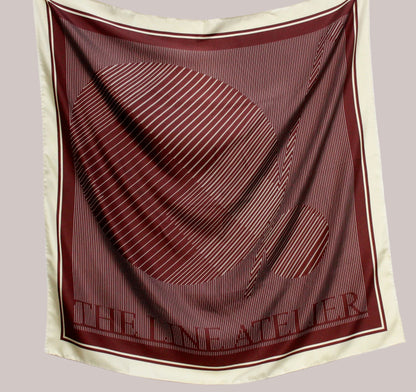 Maroon and beige scarf with 'The Line Atelier' branding on a light gray background