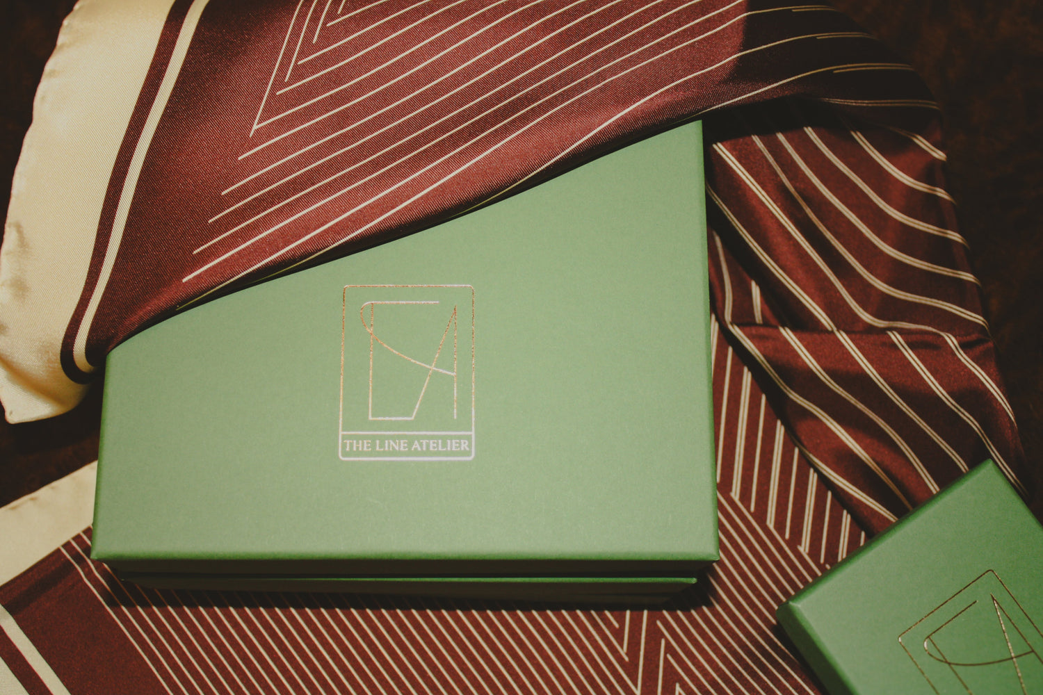 Rogues Equilibrium large brown silk scarf draped over The Line Atelier packaging