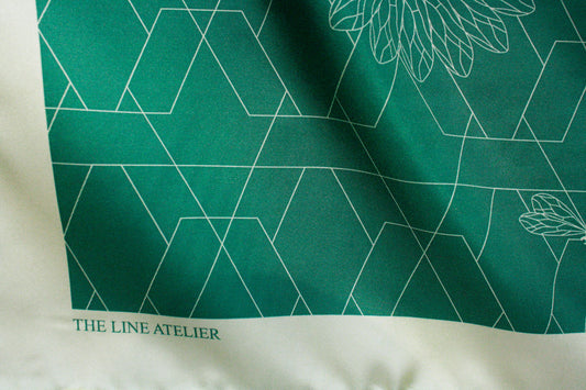 Green silk scarf with geometric patterns and 'The Line Atelier' branding on a white background