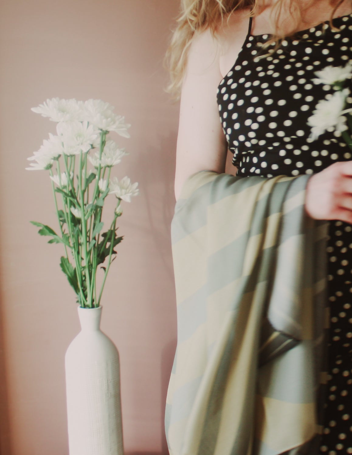Model holding Willow Grove Wool & Silk Scarf by The Line Atelier next to a vase with white flowers against a pink wall